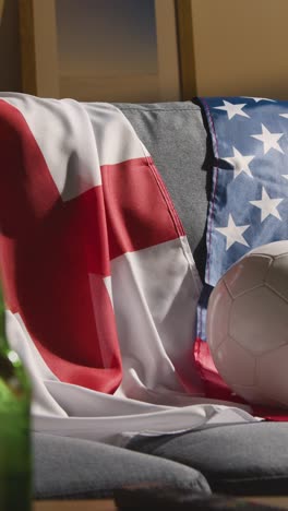 Vertical-Video-Of-Sofa-In-Lounge-With-English-And-American-Flags-And-Ball-As-Fans-Prepare-To-Watch-Football-Soccer-Match-On-TV